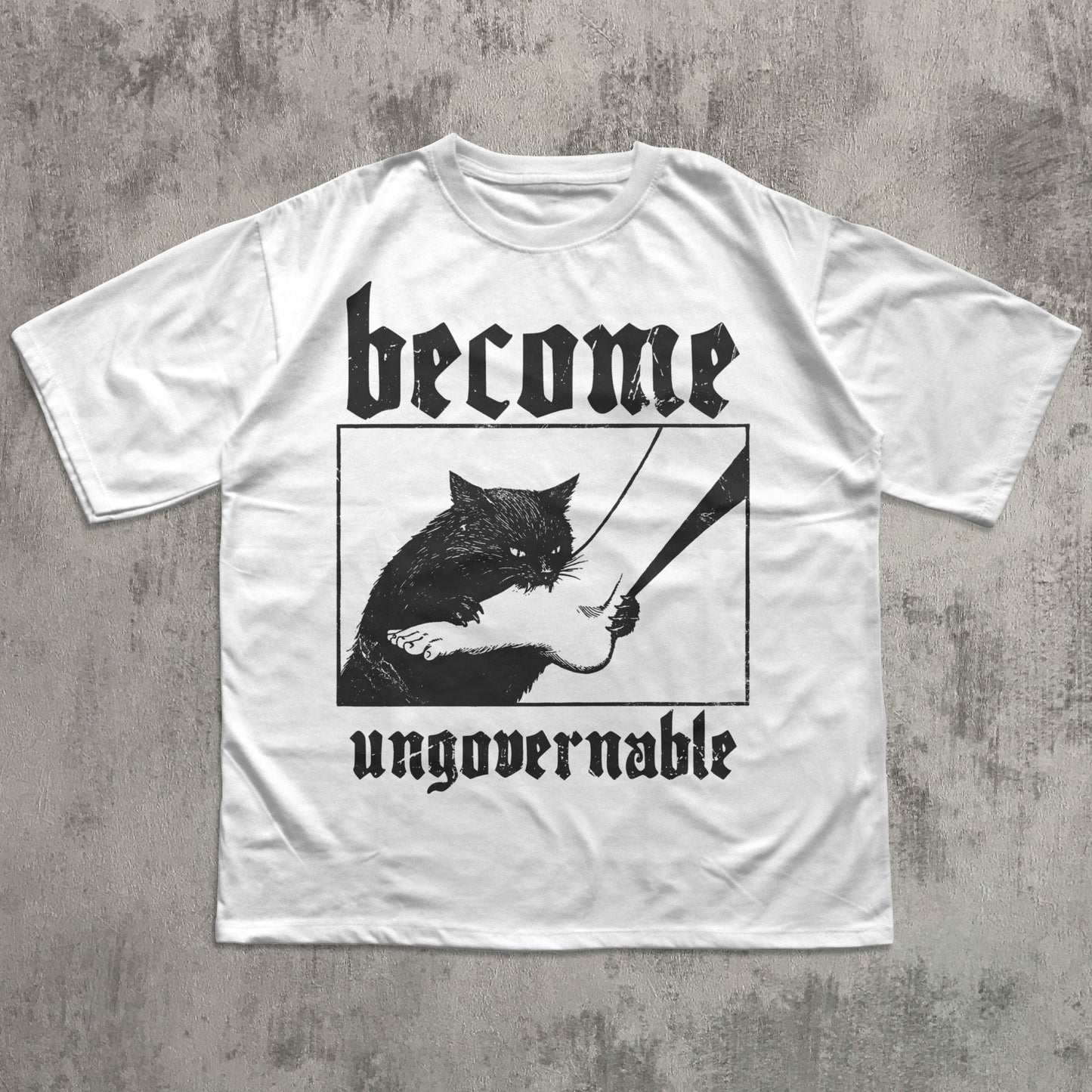 White t-shirt with black graphic of a cat holding a sword and text 'become ungovernable' on a concrete surface.