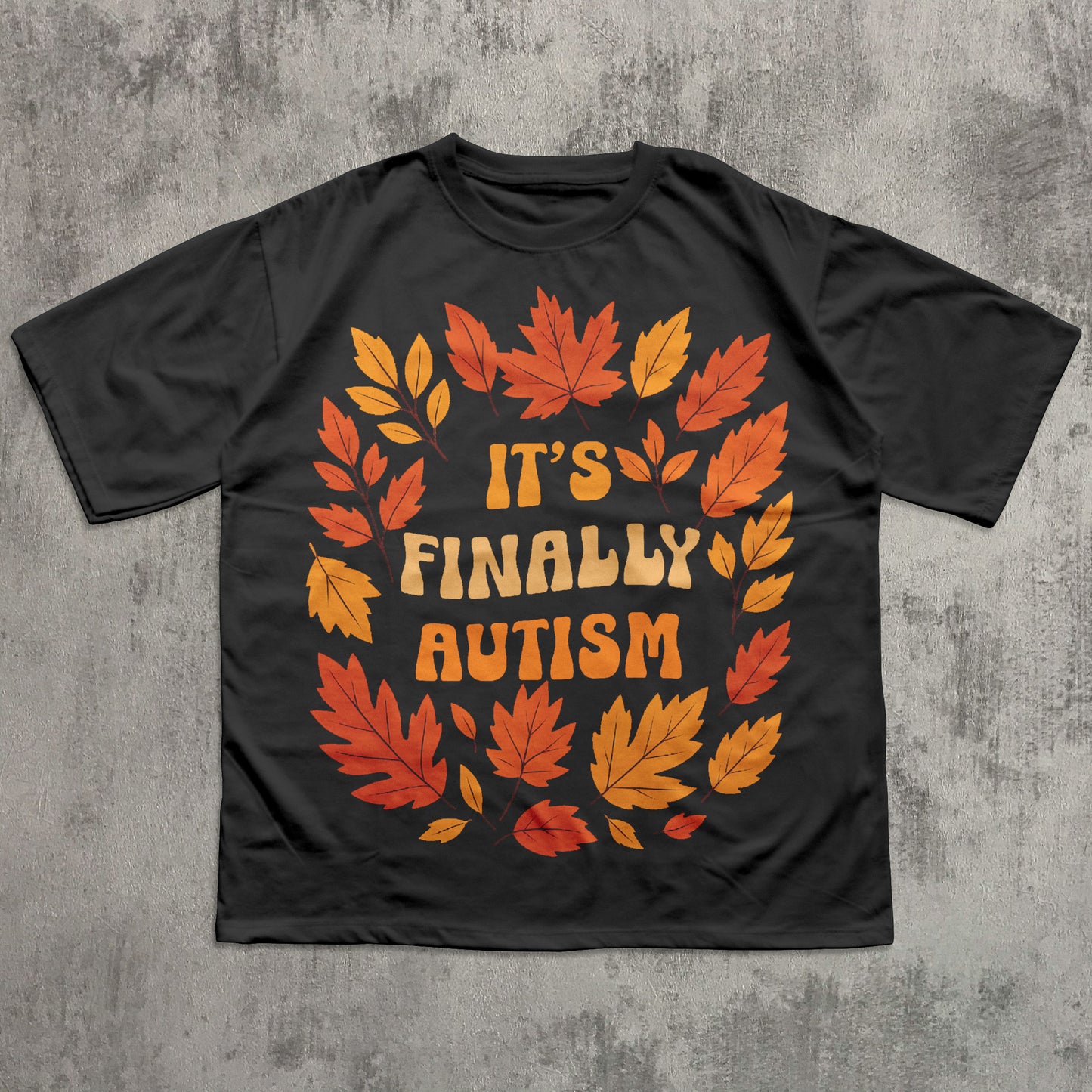 Black t-shirt with autumn leaf design and 'It's Finally Autism' text on a textured gray background