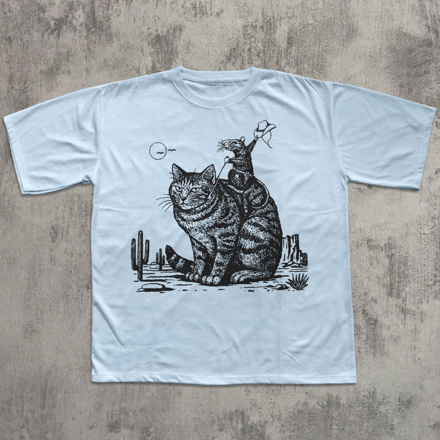 Light blue t-shirt with a black and white graphic of a cat and a skeleton on a concrete surface