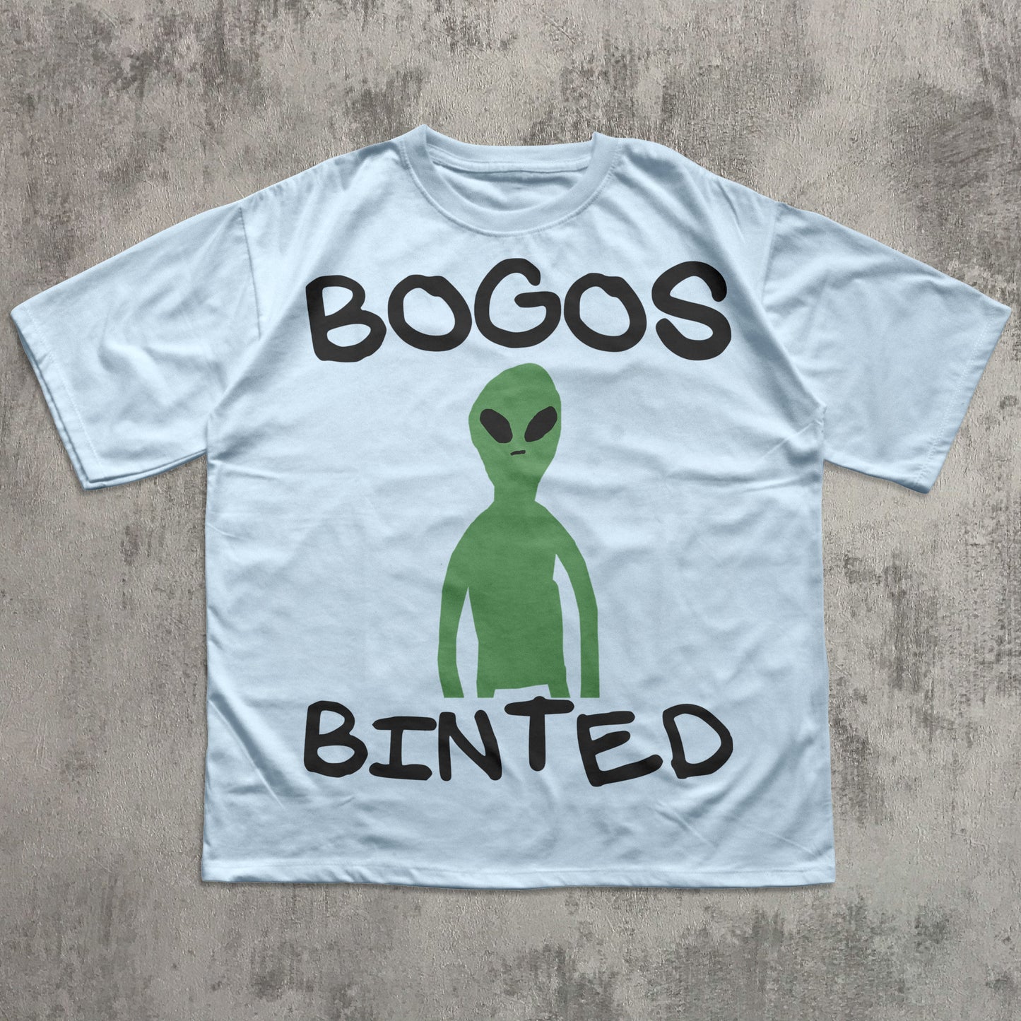 Light blue t-shirt with green alien graphic and text 'BOGOS BINTED' on a concrete surface