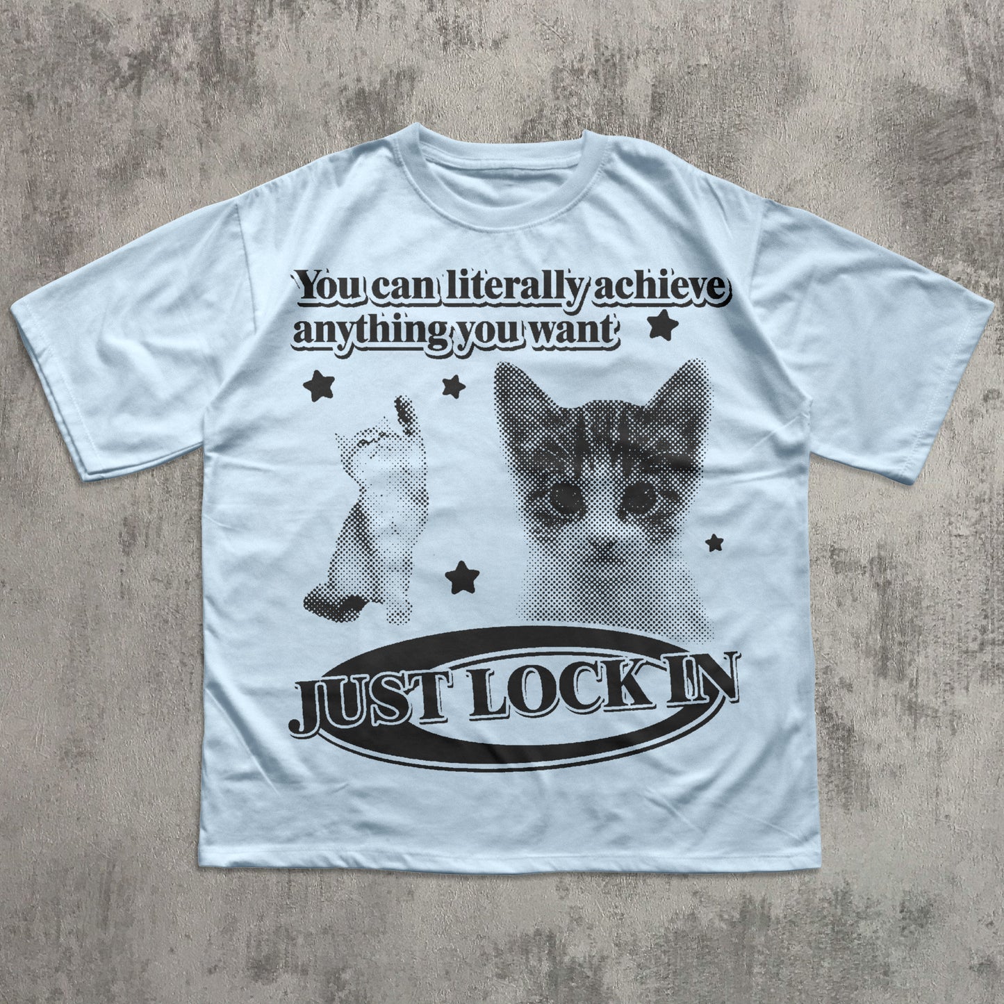 White t-shirt with a graphic of a cat and motivational text on a concrete surface