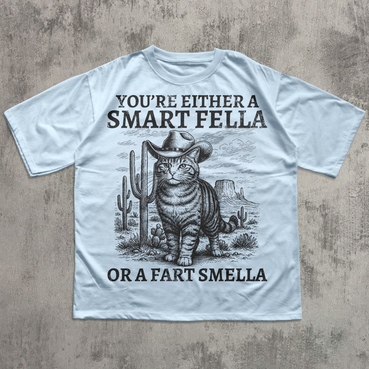 Light blue t-shirt with a graphic of a cat in a cowboy hat and text on a concrete surface