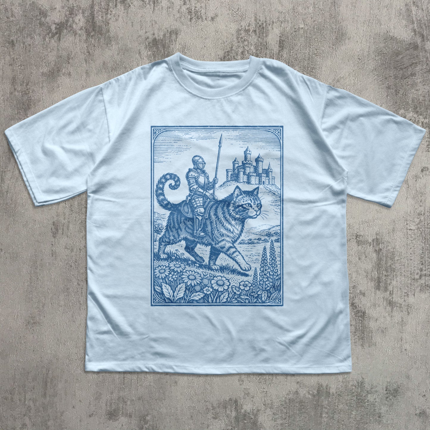 Light blue t-shirt with a blue graphic design of a knight on a tiger, castle, and landscape on a concrete surface.