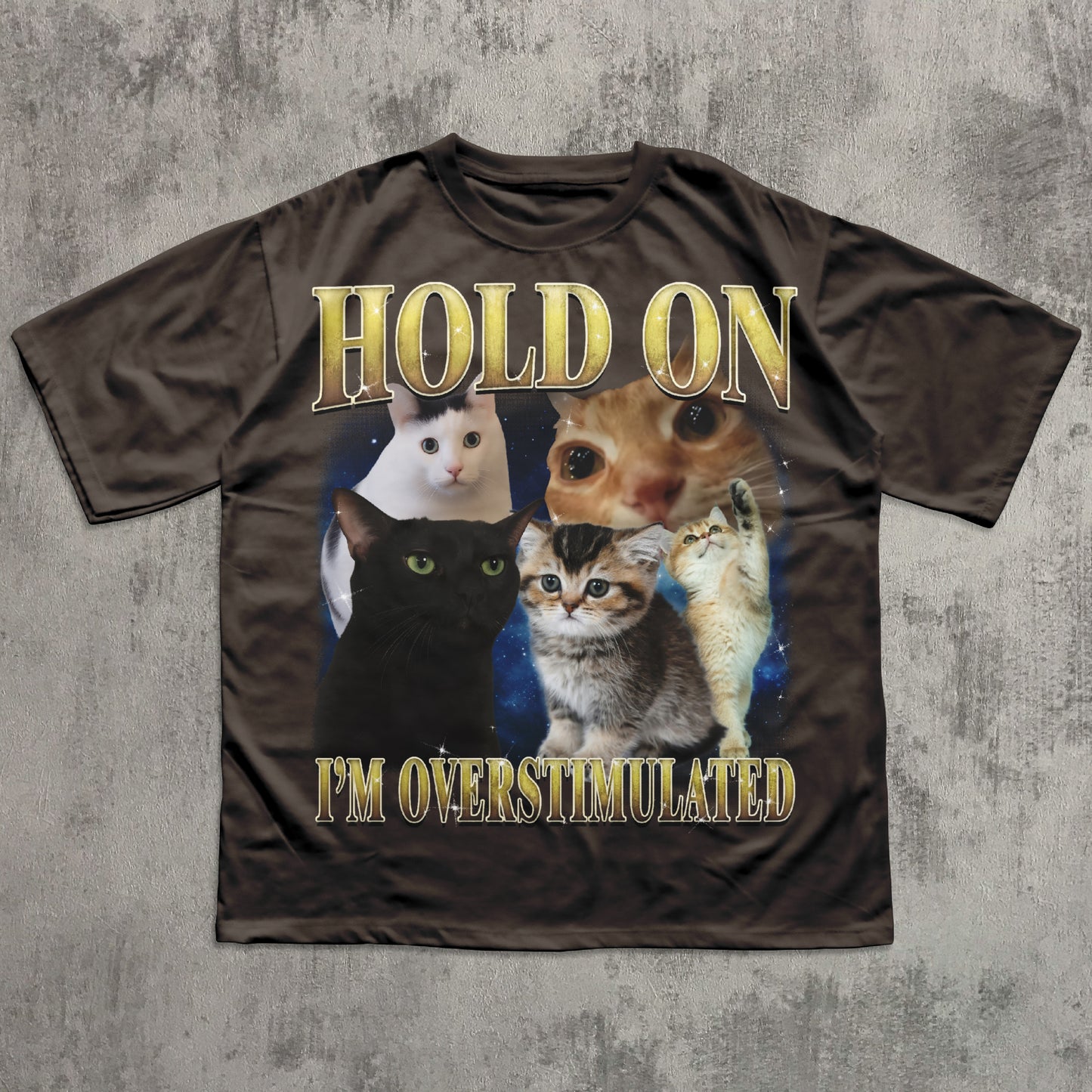 Brown t-shirt with cat graphic and text 'Hold on I'm overstimulated' on a textured gray background