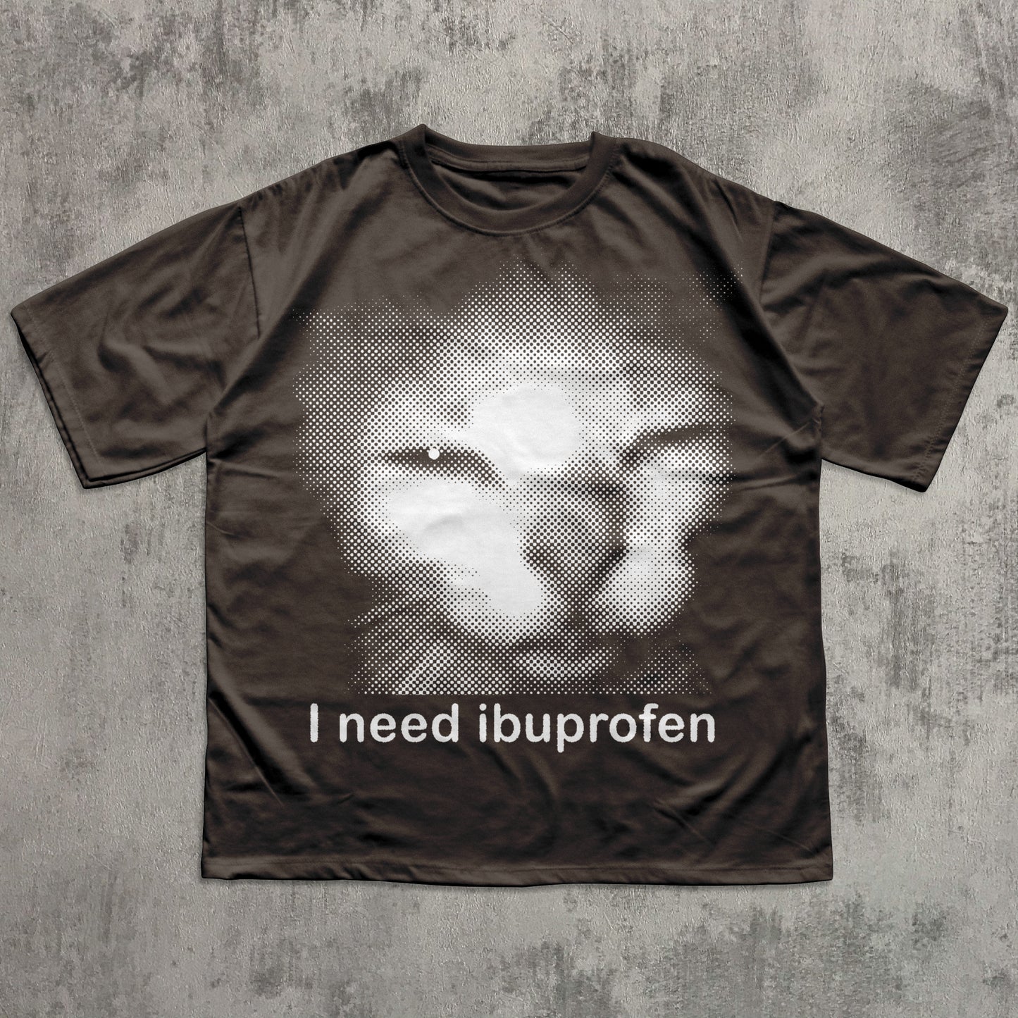 Brown t-shirt with a graphic of a face and 'I need ibuprofen' text on a textured gray background