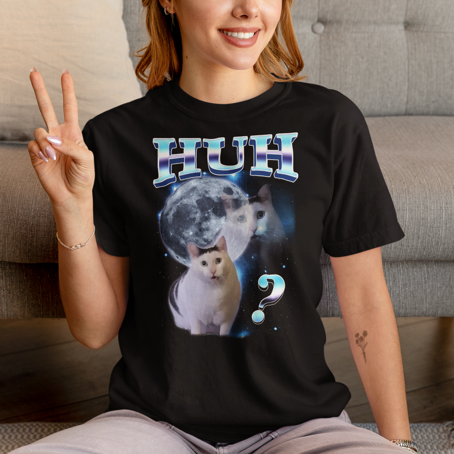 Person wearing a black t-shirt with a cat graphic and text, sitting on a couch.