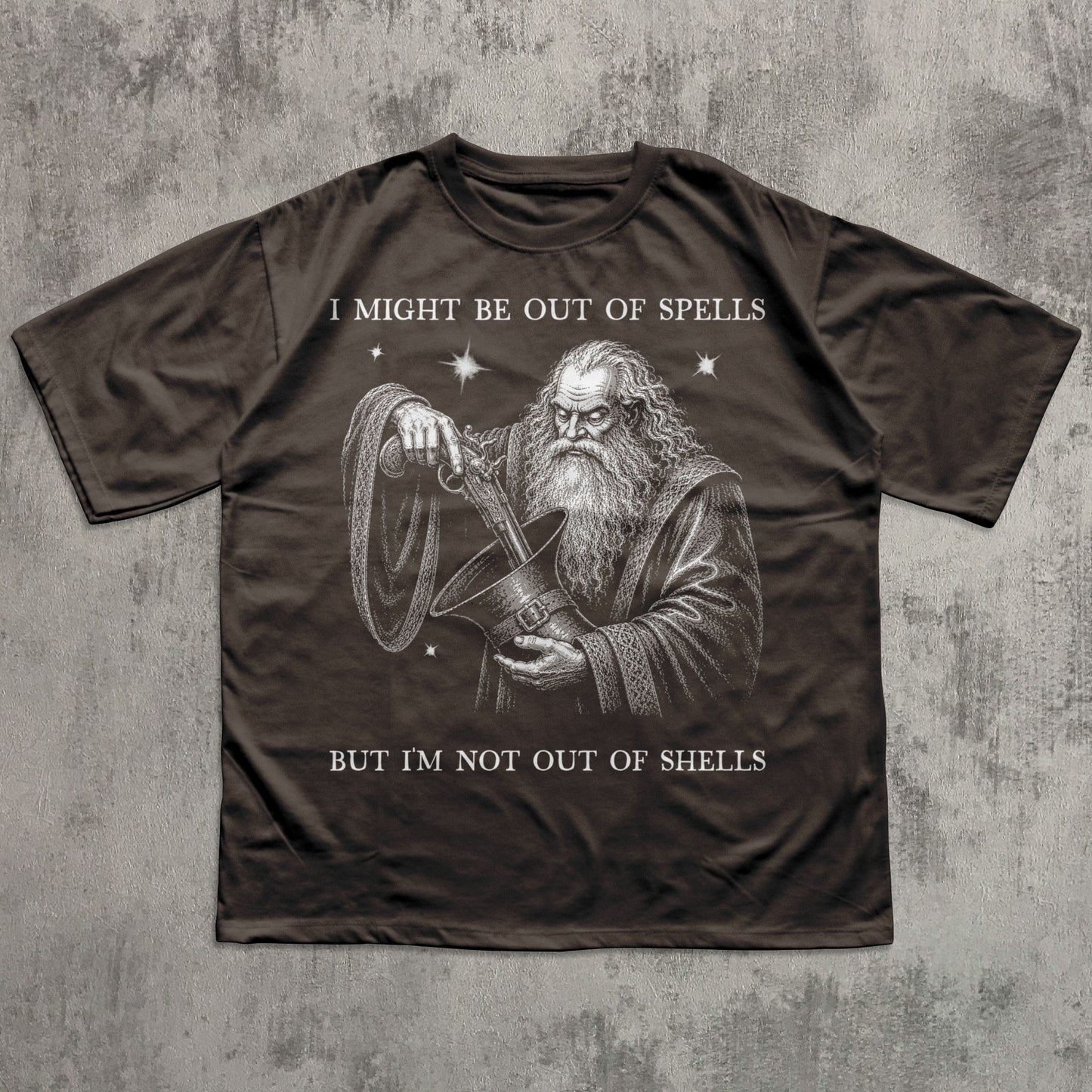 A dark brown short-sleeve t-shirt with a graphic of a wizard holding a shell, with the text 'I MIGHT BE OUT OF SPELLS BUT I'M NOT OUT OF SHELLS' printed in white, laid flat on a textured gray background.