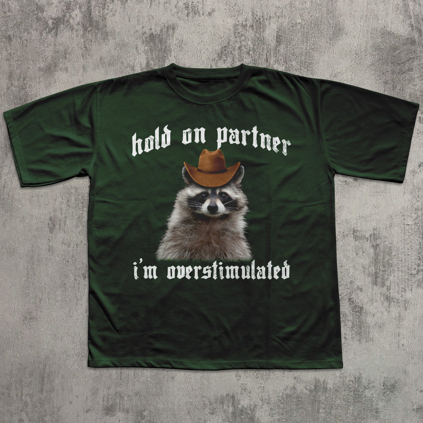 Green t-shirt with a raccoon wearing a cowboy hat and text on a concrete background