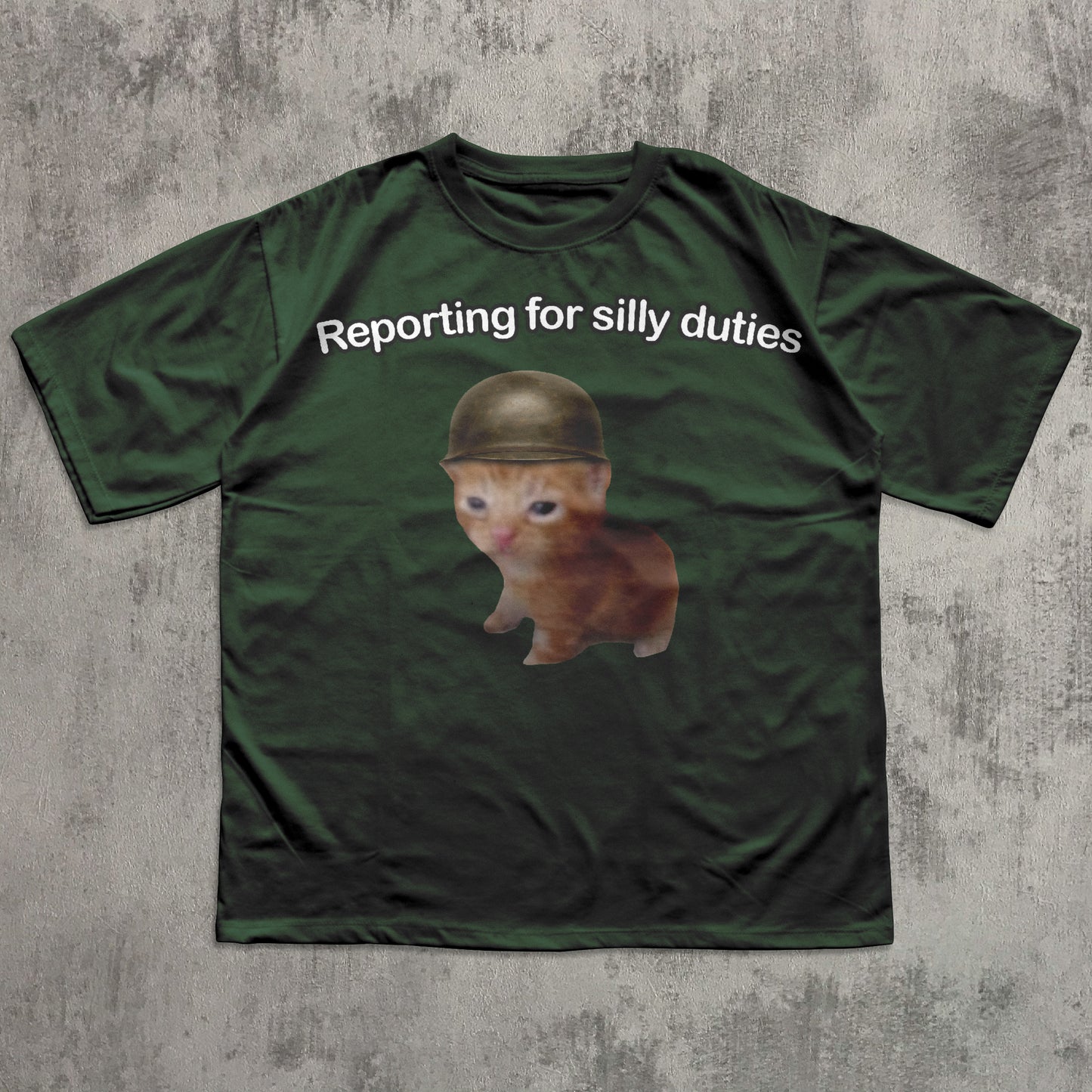 Green t-shirt with a cat wearing a helmet and text 'Reporting for silly duties' on a concrete surface.