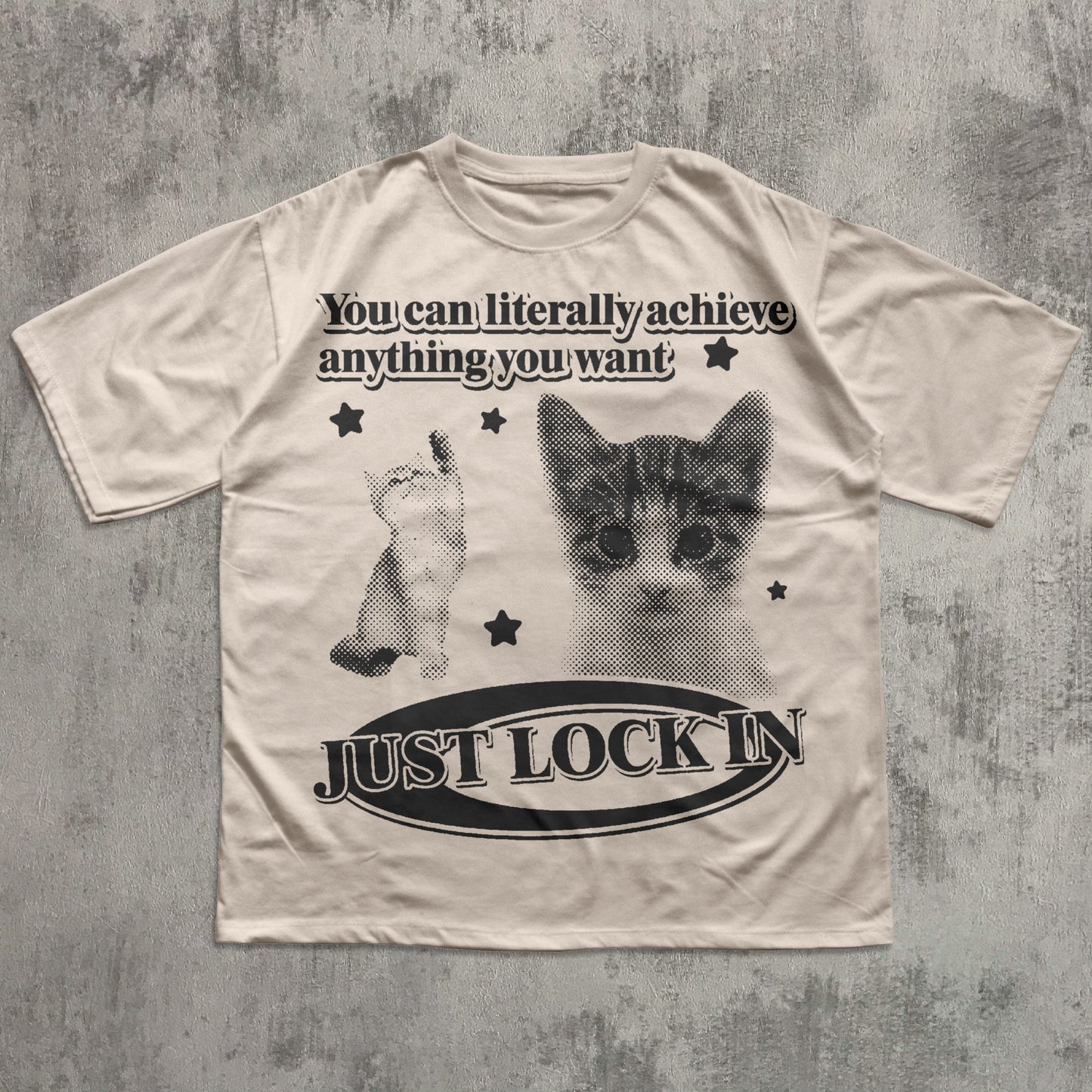 Beige t-shirt with cat graphic and motivational text on a textured gray background