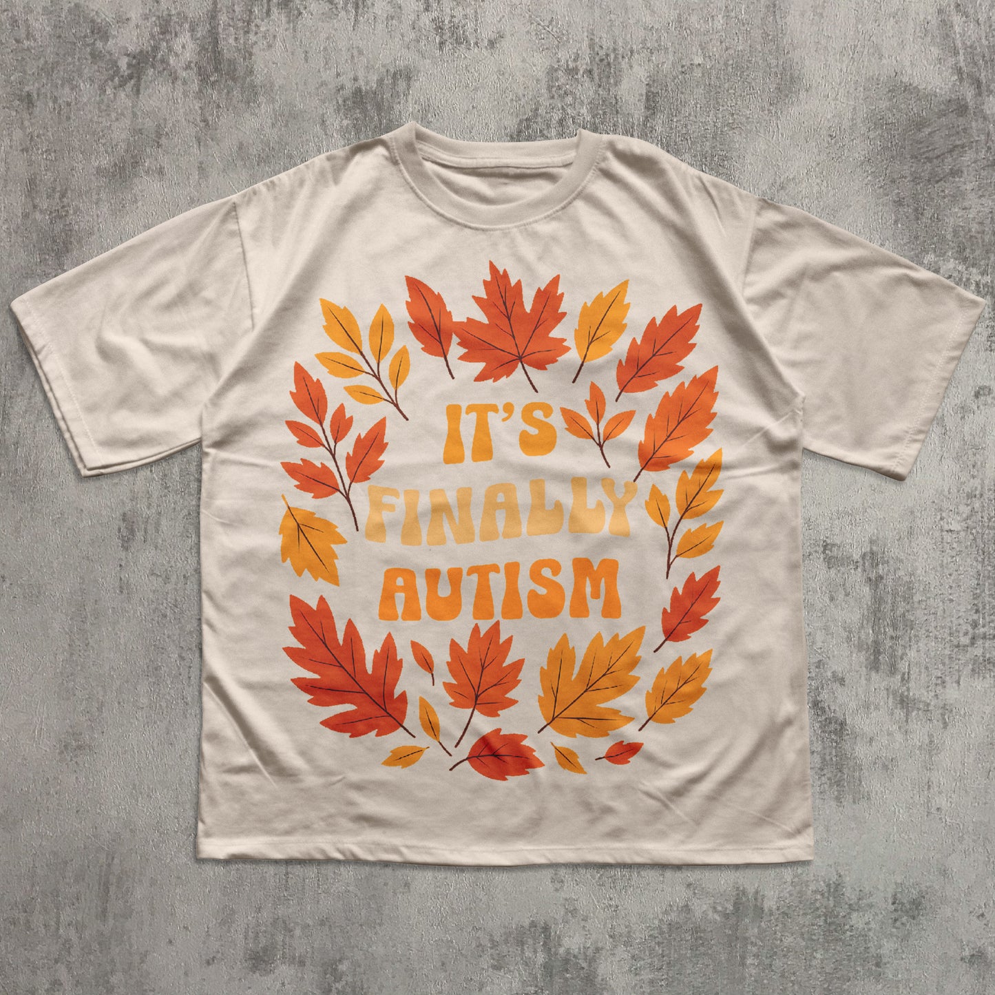 T-shirt with autumn leaf design and 'It's Finally Autism' text on a textured gray background
