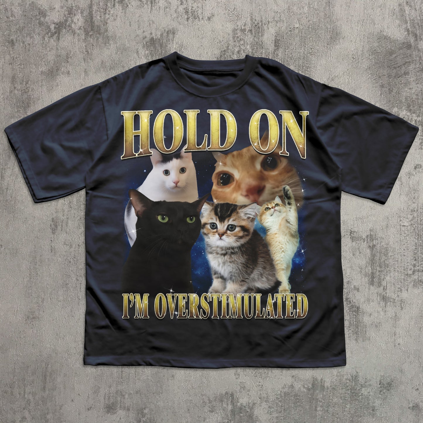 Black t-shirt with cartoon cats and text 'Hold on I'm overstimulated' on a textured gray background
