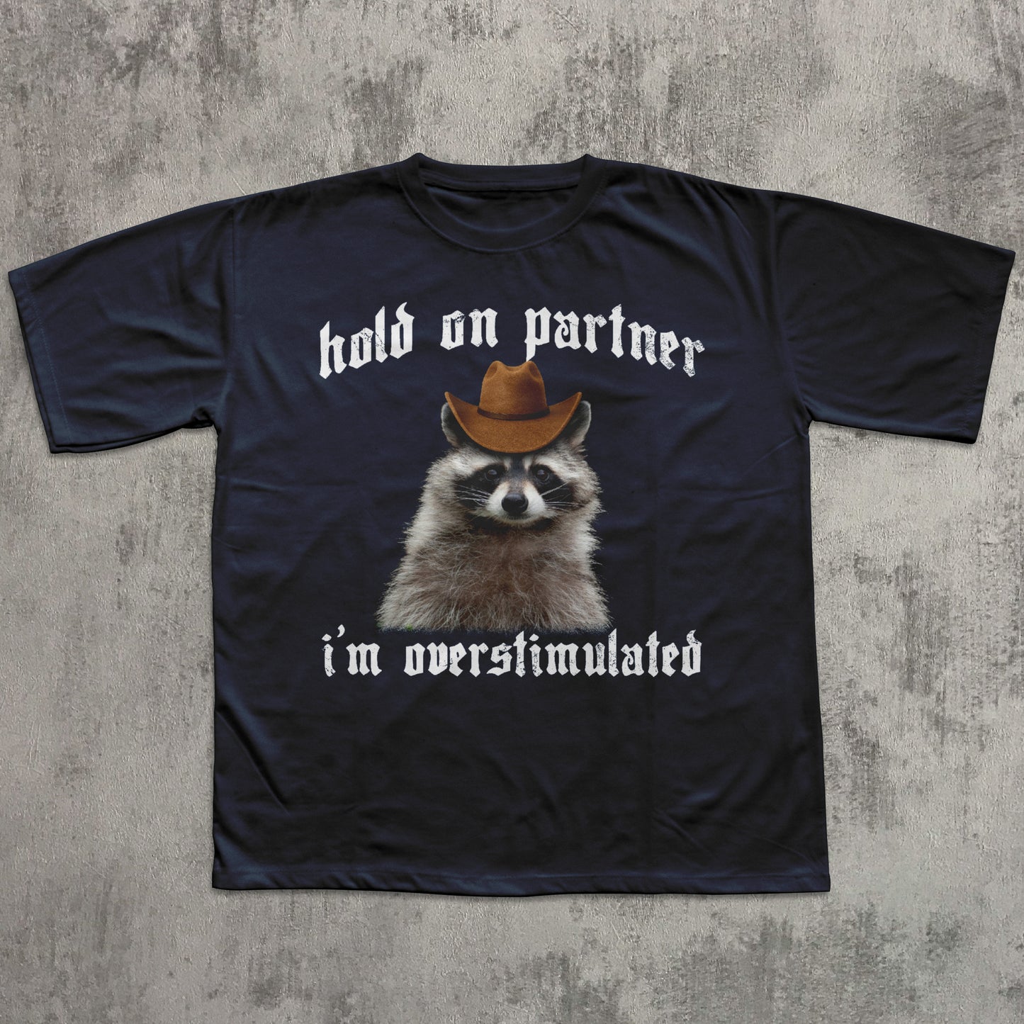 Black t-shirt with a raccoon wearing a cowboy hat and text on a concrete surface