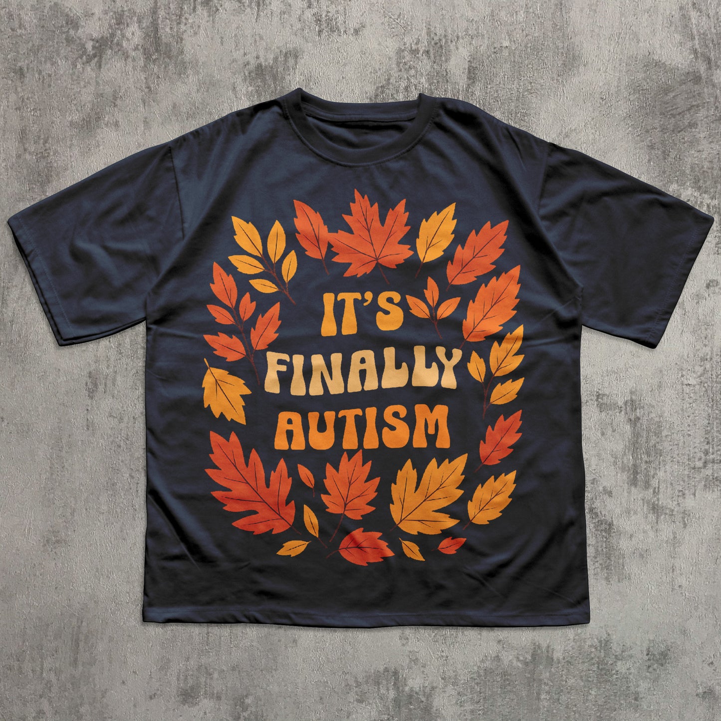 Black t-shirt with autumn leaf design and 'It's Finally Autism' text on a concrete surface