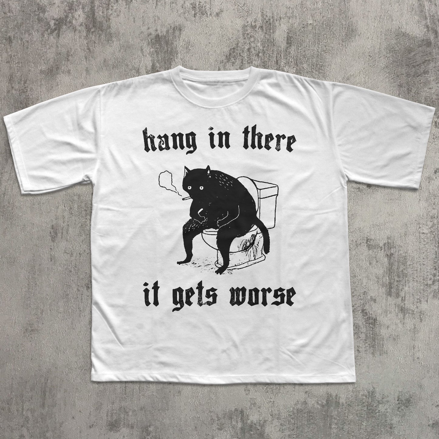 White t-shirt with black cat graphic and text 'hang in there it gets worse' on a textured gray background