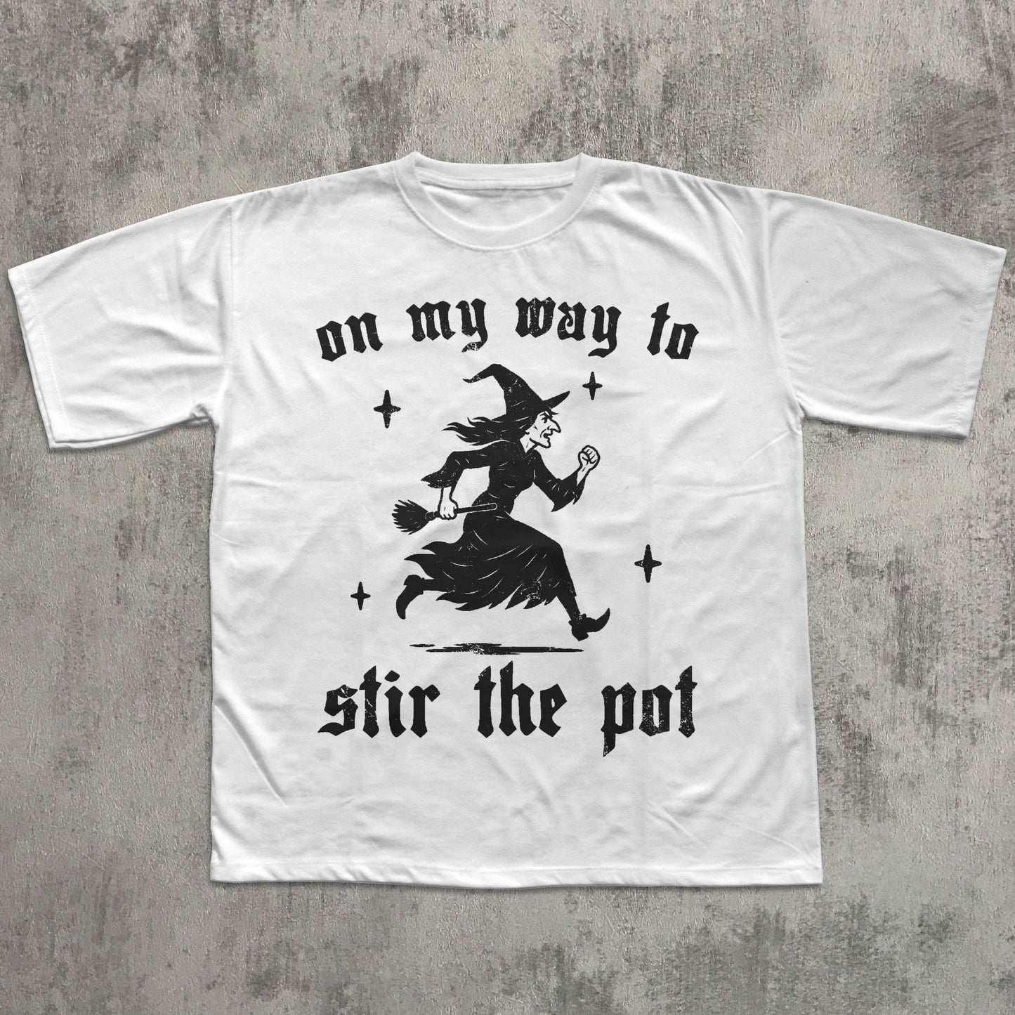 White t-shirt with black witch graphic and text on a gray concrete background