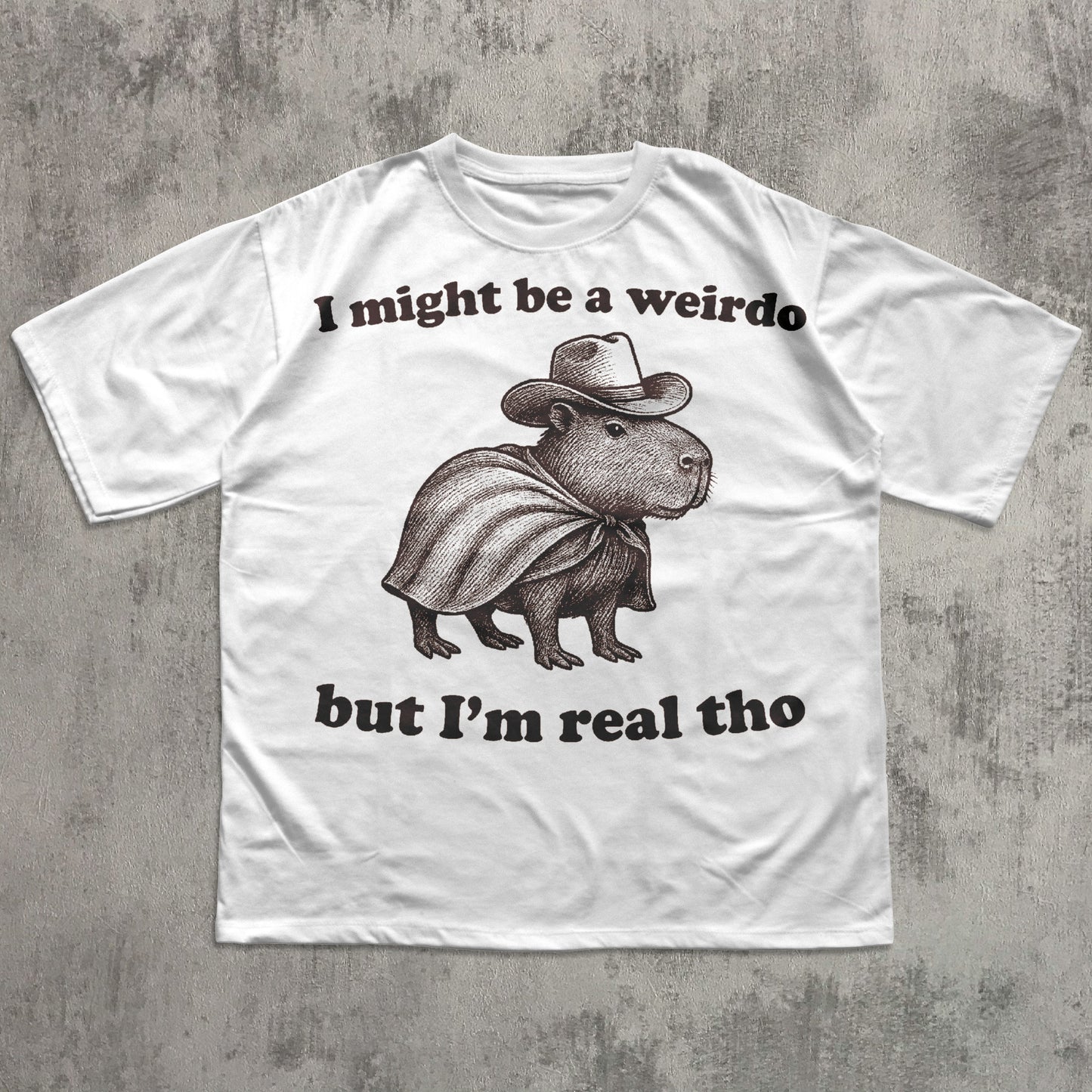 White funny t-shirt with a graphic of a capybara wearing a cowboy hat and text on a concrete surface