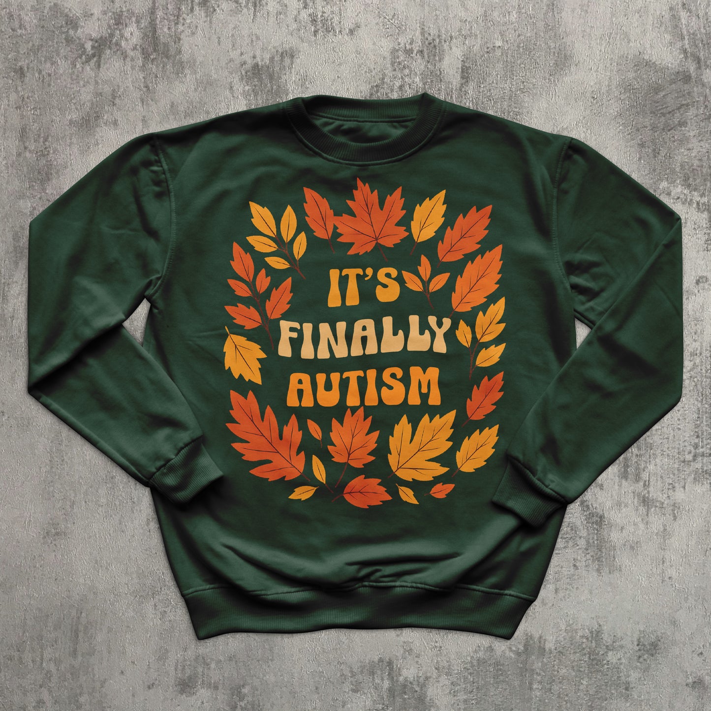 Green sweatshirt with autumn leaf design and 'It's Finally Autism' text on a gray textured background