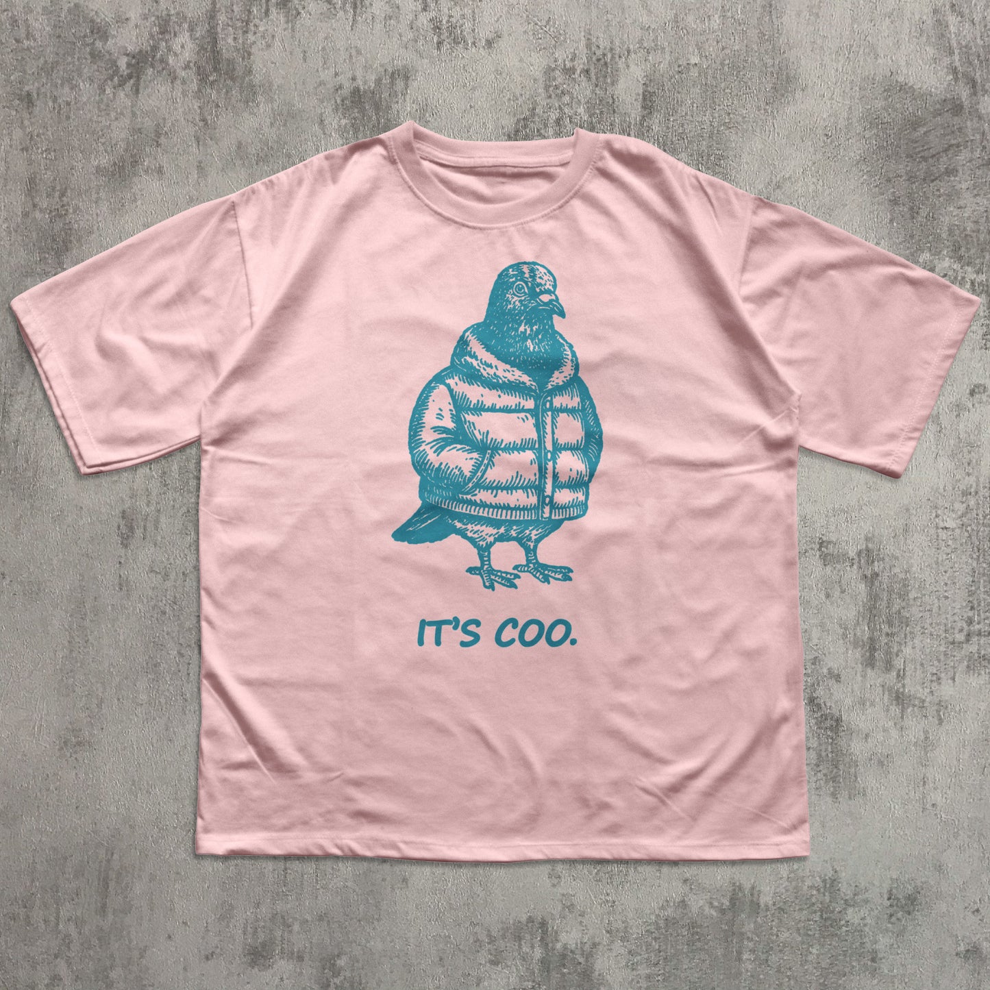 Pink t-shirt with a blue penguin graphic and 'it's coo.' text on a textured gray background