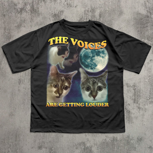 Black t-shirt with cat graphic and text 'The Voices Are Getting Louder' on a textured gray background