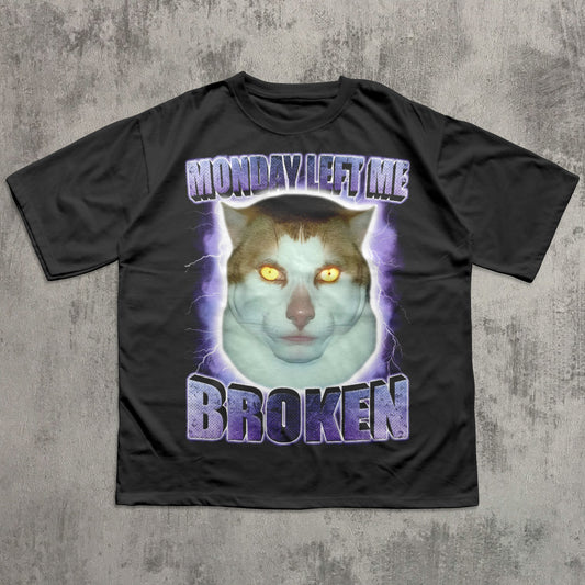 Black funny t-shirt with a graphic of a cat and text 'Monday Left Me Broken' on a textured gray background