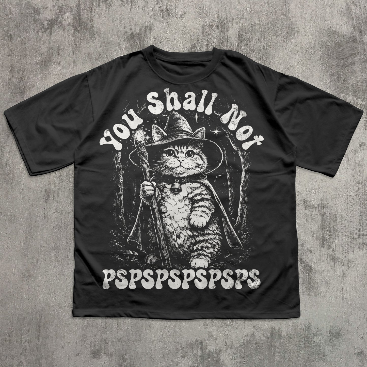Black t-shirt with a cat in a wizard hat graphic and text on a concrete background