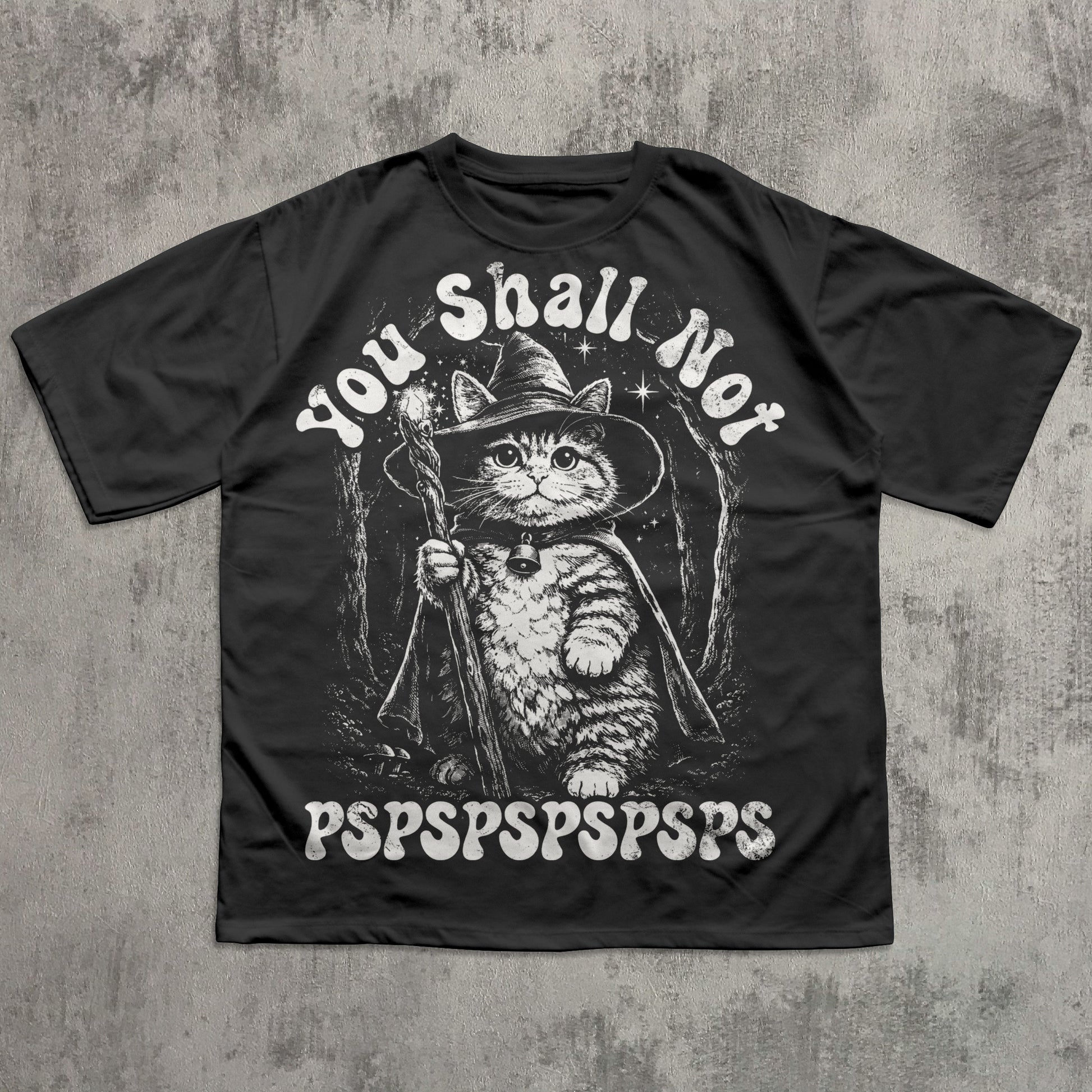 Black t-shirt with a cat in a wizard hat graphic and text on a concrete background