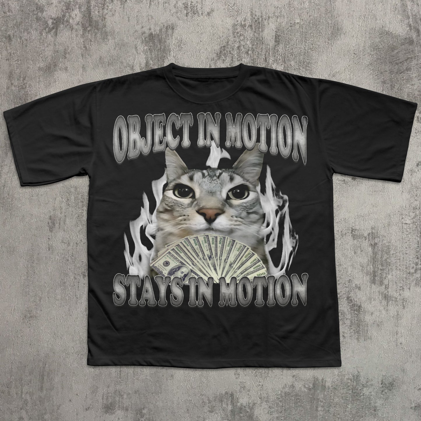 Black t-shirt with a graphic of a cat holding money and text 'OBJECT IN MOTION STAYS IN MOTION' on a textured gray background.