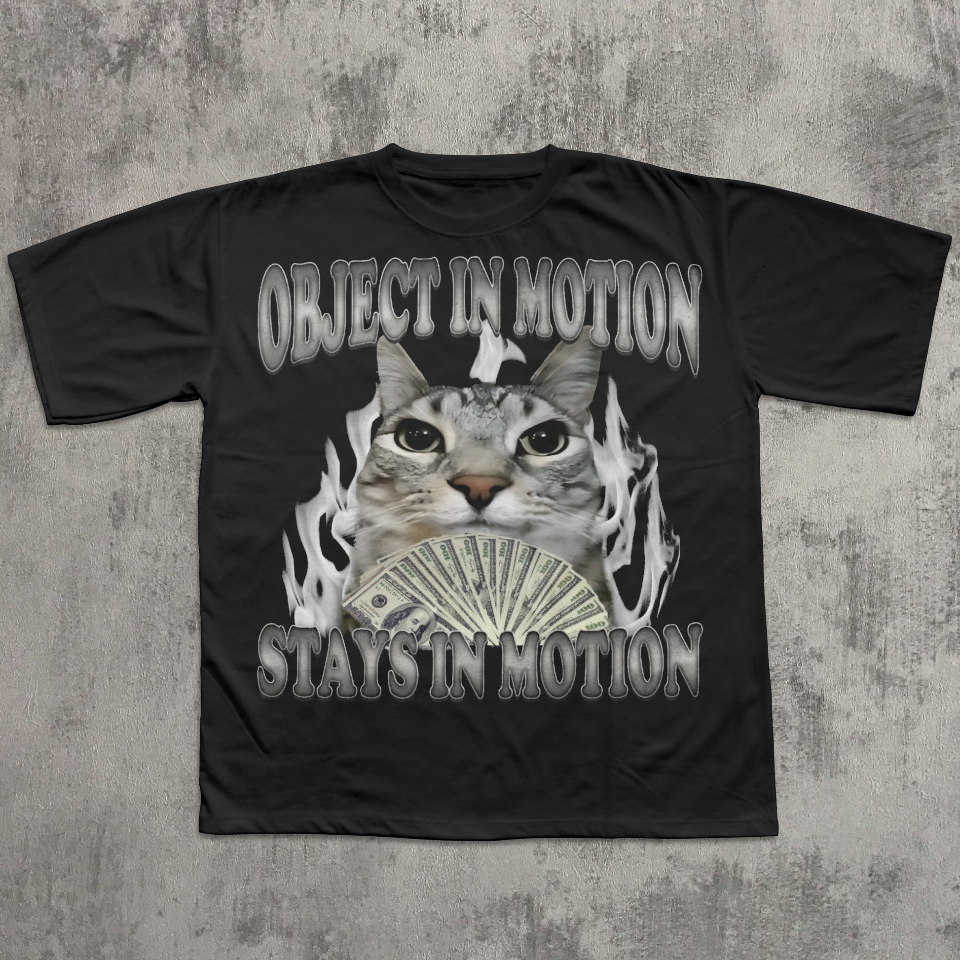 Black t-shirt with a graphic of a cat holding money and text 'OBJECT IN MOTION STAYS IN MOTION' on a textured gray background.