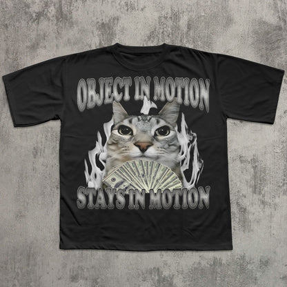 Black t-shirt with a graphic of a cat holding money and text 'OBJECT IN MOTION STAYS IN MOTION' on a textured gray background.