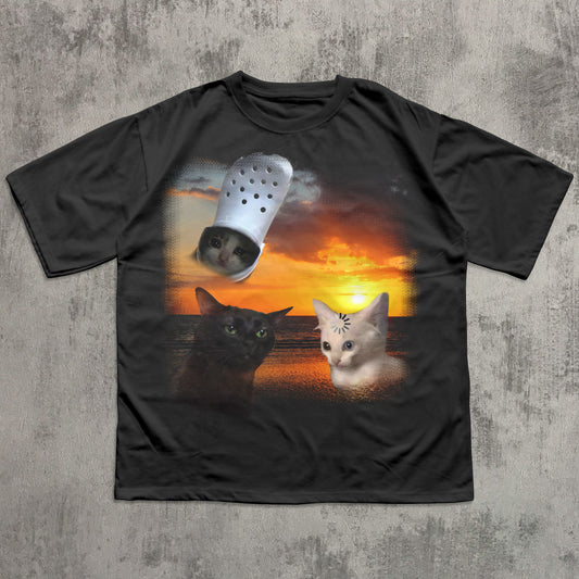 Black t-shirt with a graphic of two cats and a Croc shoe on a sunset background