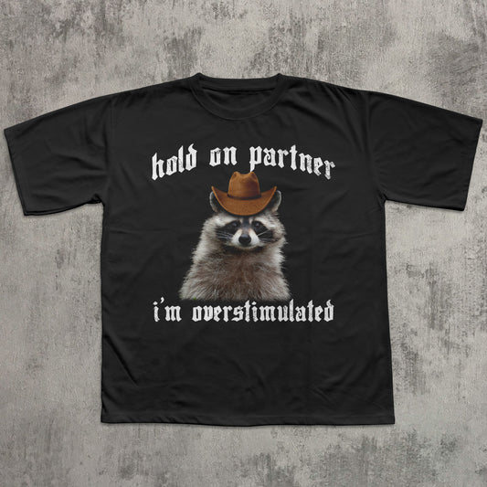 Black t-shirt with a raccoon wearing a cowboy hat and text on a textured gray background