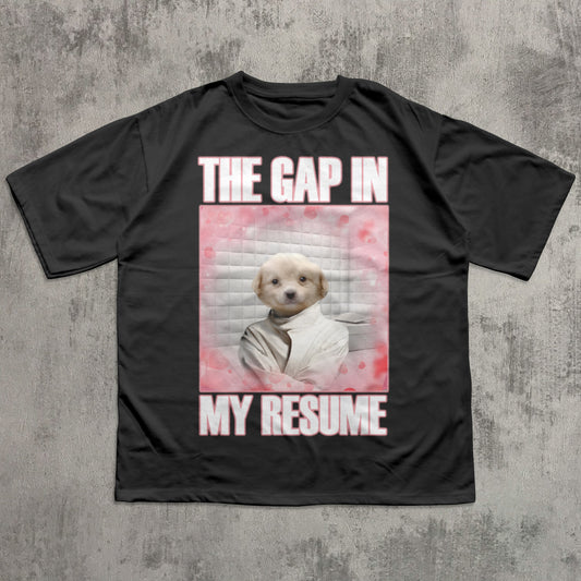 Black t-shirt with a graphic of a dog and text 'The gap in my resume' on a concrete surface.