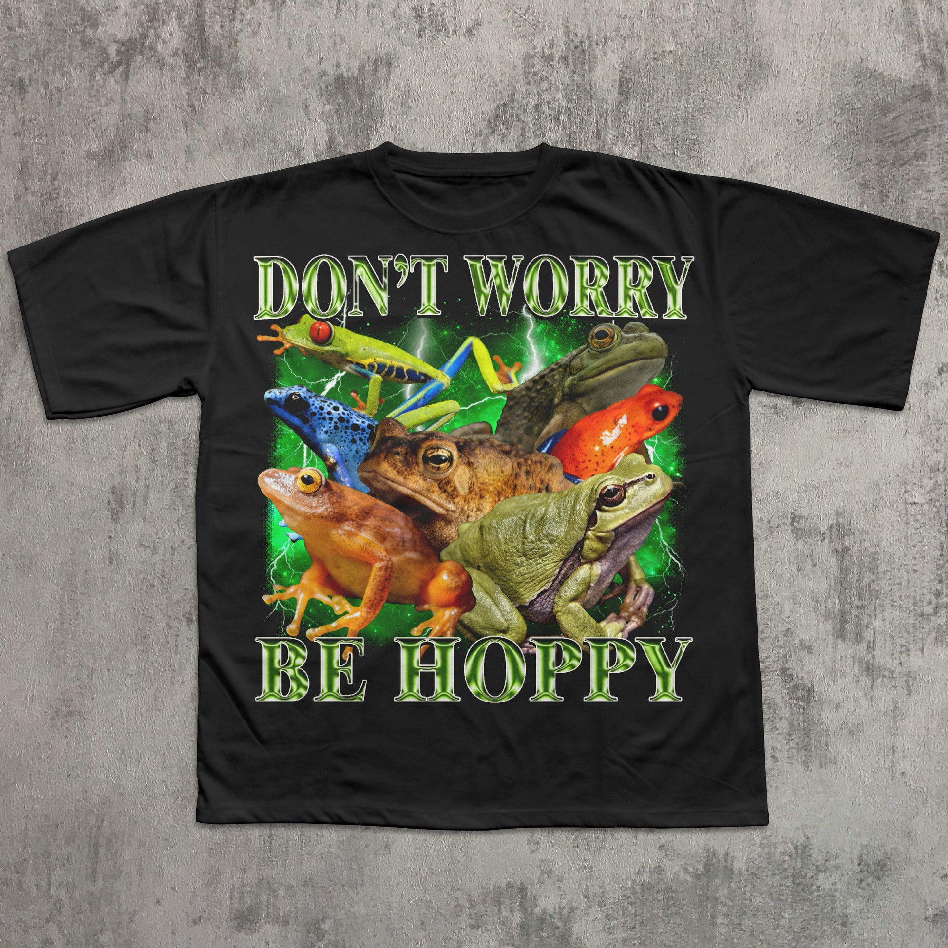 Black t-shirt with colorful frogs and text 'Don't Worry Be Hoppy' on a concrete background