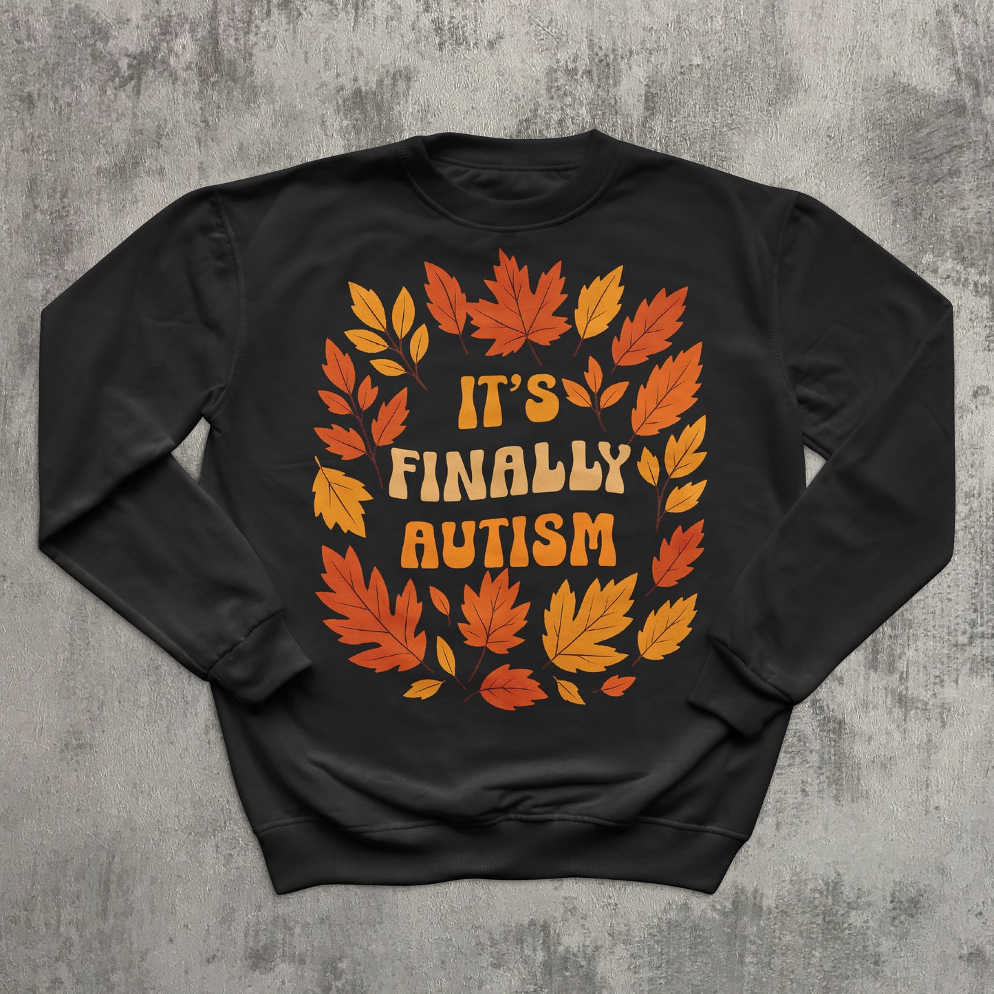 Black sweatshirt with autumn leaf design and 'It's Finally Autism' text on a textured gray background
