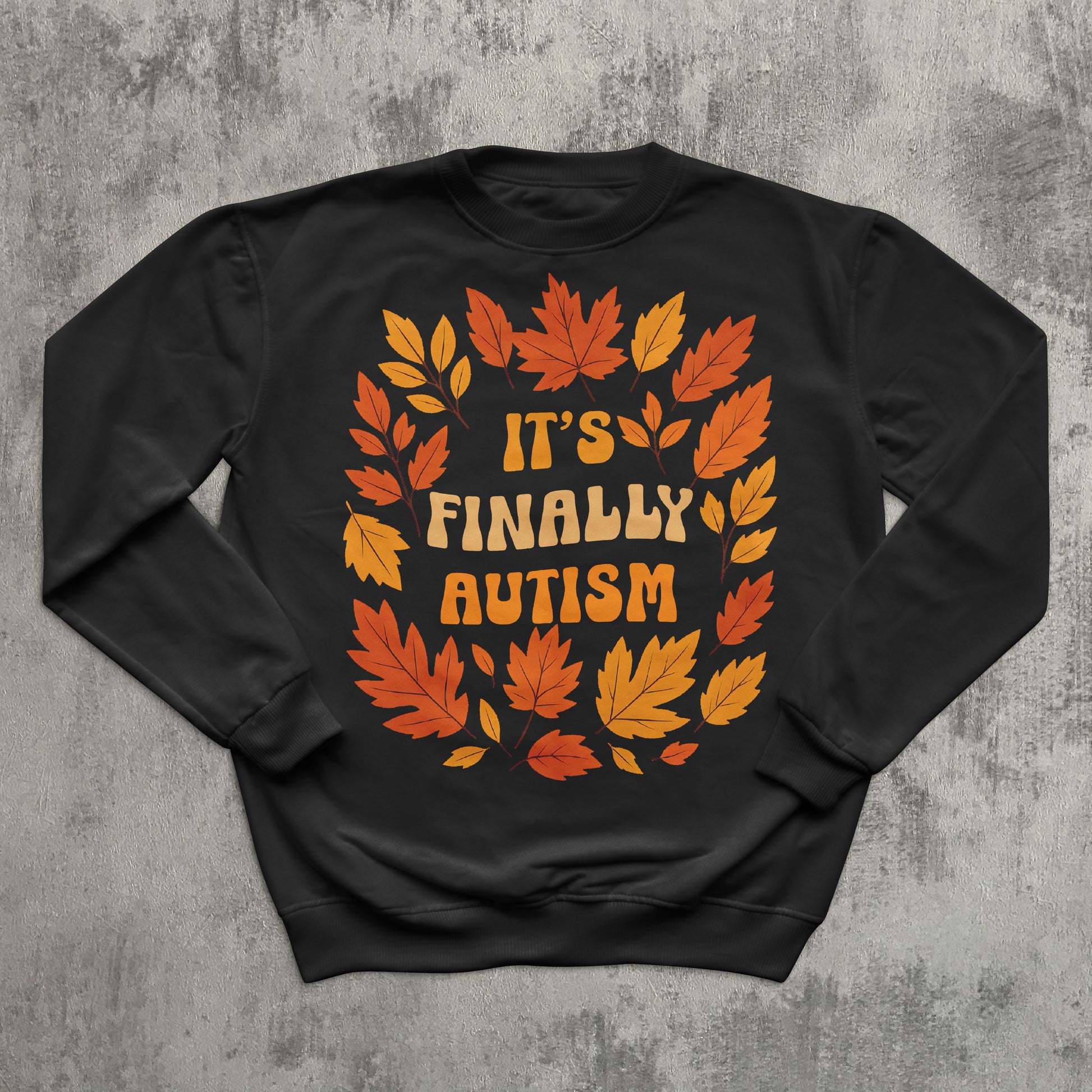 Black sweatshirt with autumn leaf design and 'It's Finally Autism' text on a textured gray background