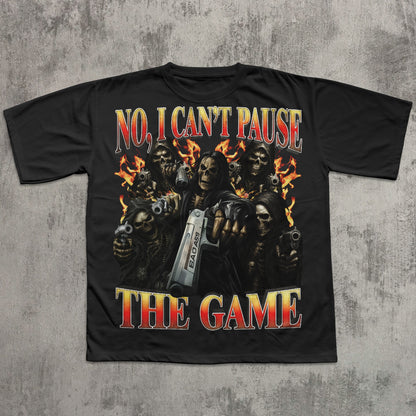 black t-shirt with graphic design of skeletons holding guns and a console, text 'No, I Can't Pause The Game' on a textured gray background.