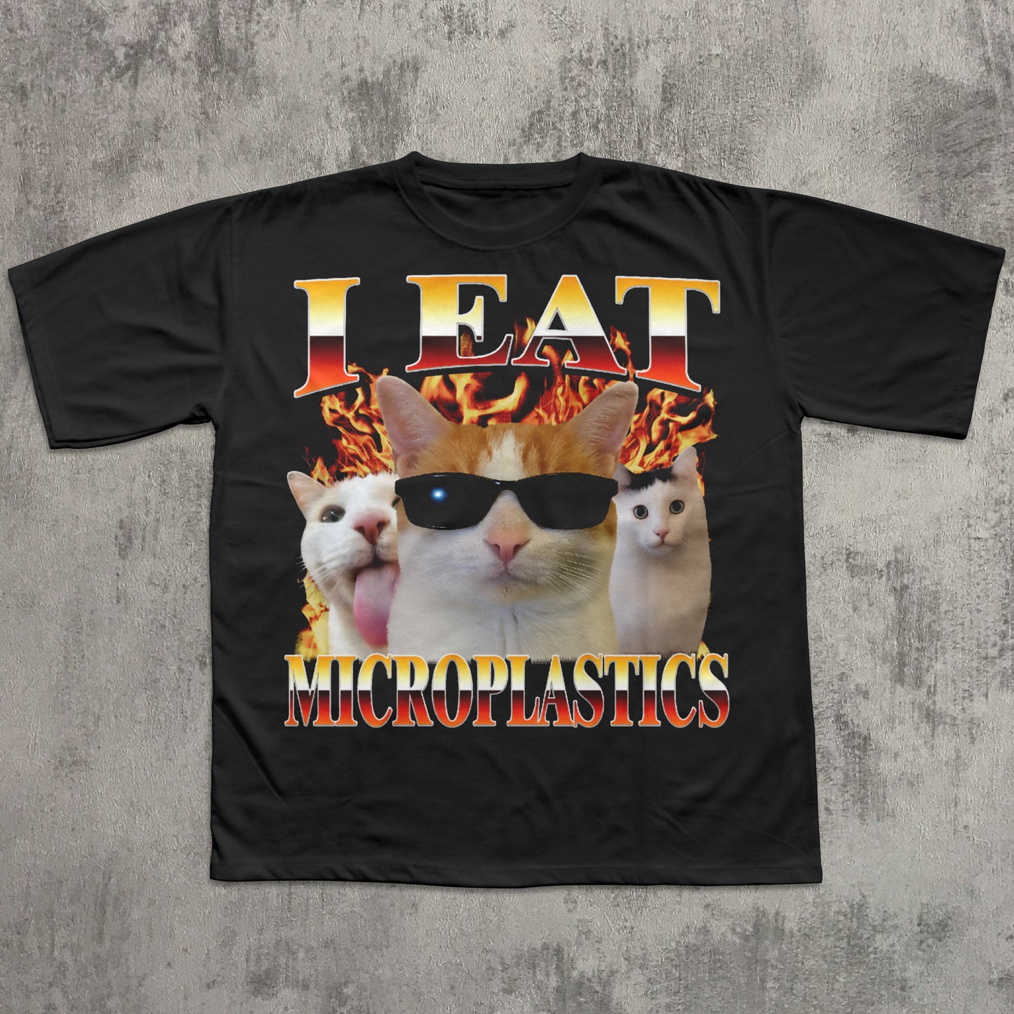 Black t-shirt with a graphic of cats wearing sunglasses and text 'I Eat Microplastics' on a concrete surface.