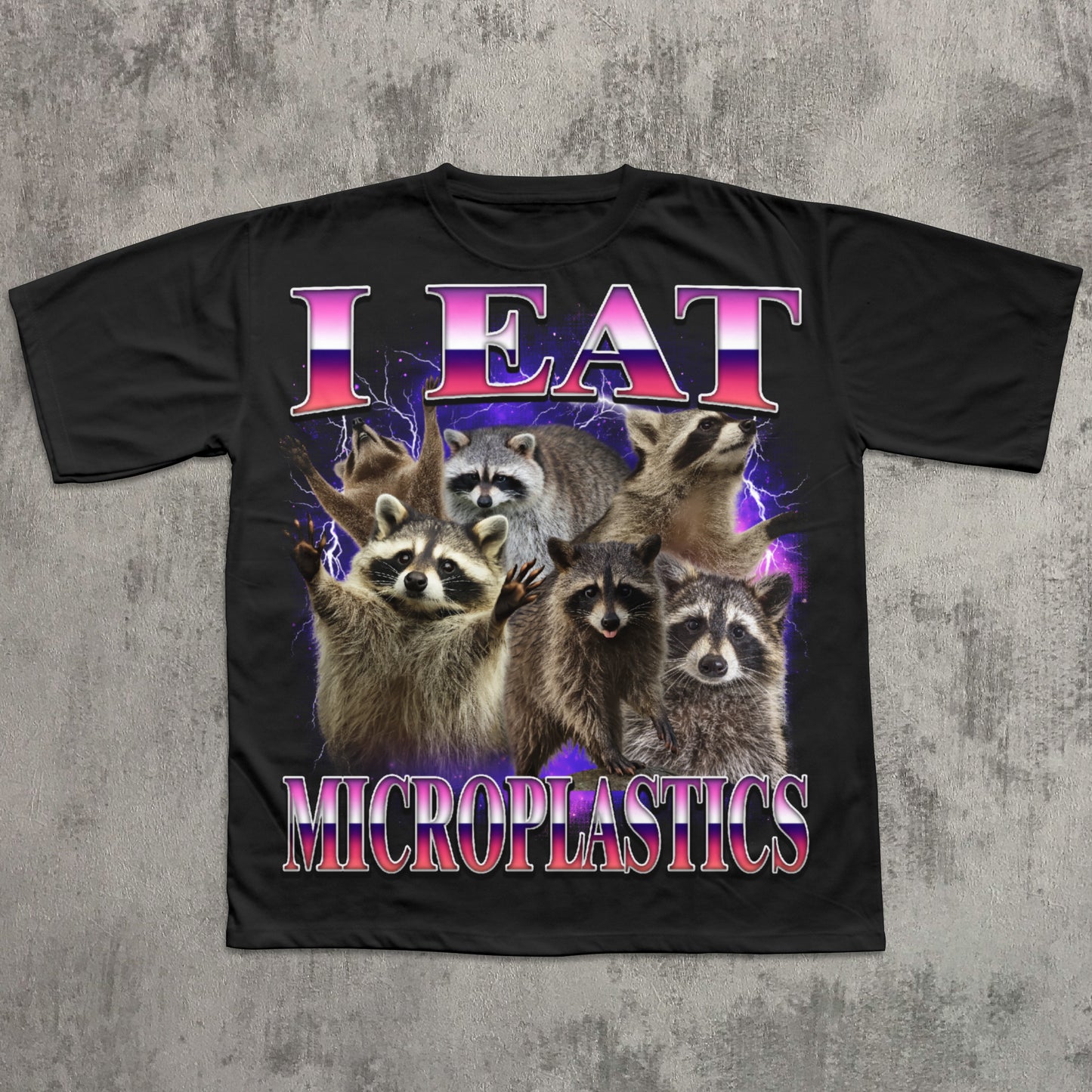 Black t-shirt with raccoons and text 'I Eat Microplastics' on a textured gray background
