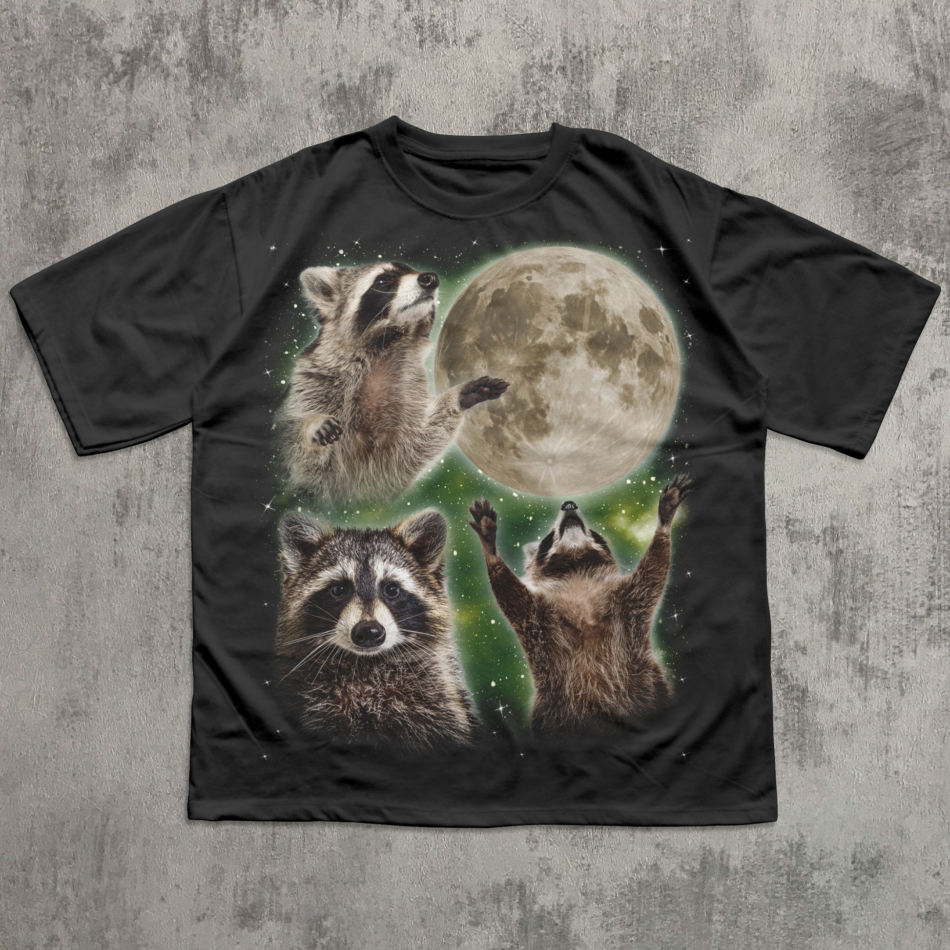 Black t-shirt with raccoon design and moon on a textured gray background