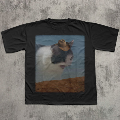 Black t-shirt with a cat wearing a cowboy hat graphic on a textured gray background