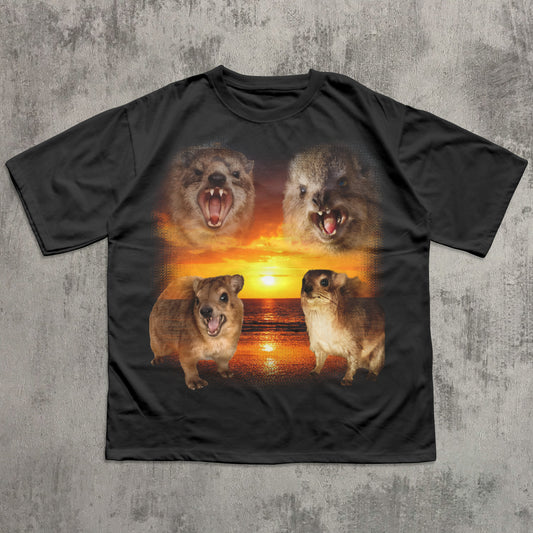 Black t-shirt with four hyrax faces on a sunset background, displayed on a textured gray surface.