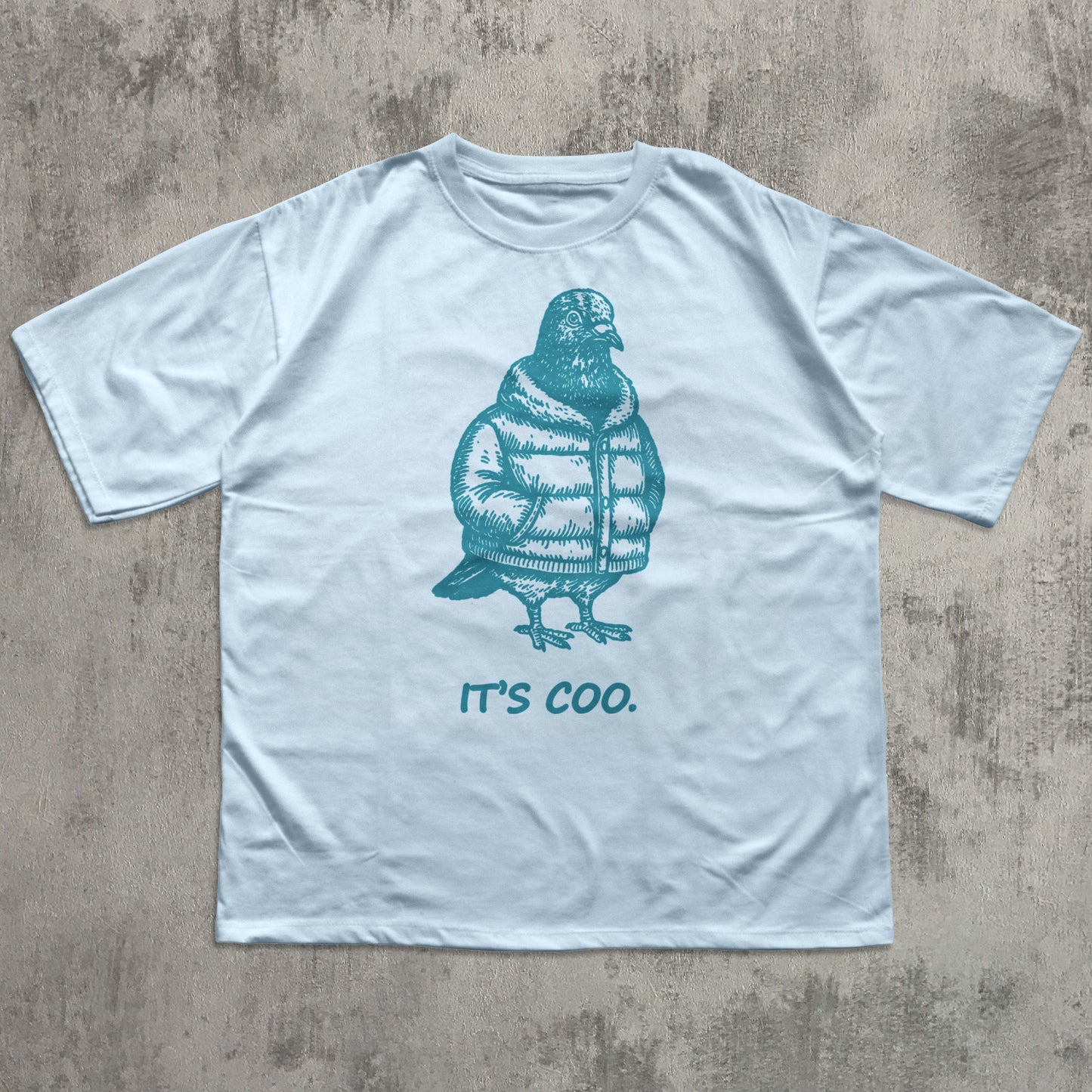 Light blue t-shirt with a teal penguin graphic and 'it's coo.' text on a textured gray background