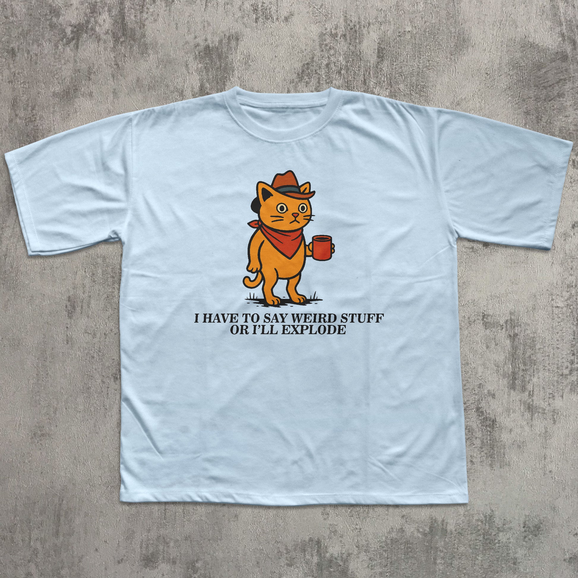 Light blue t-shirt with a cartoon cat graphic and text on a concrete surface