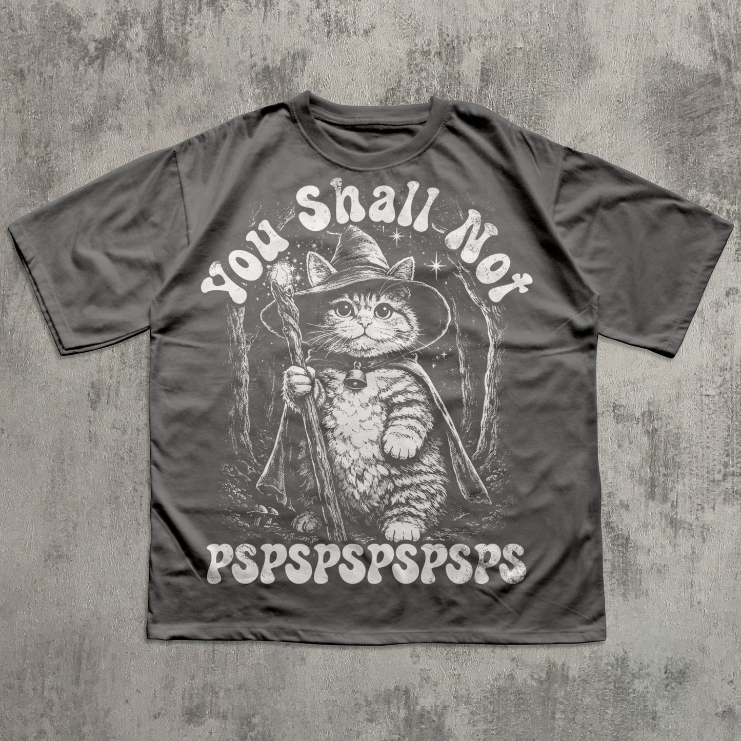 Gray t-shirt with a cat in a wizard hat graphic and text on a concrete surface