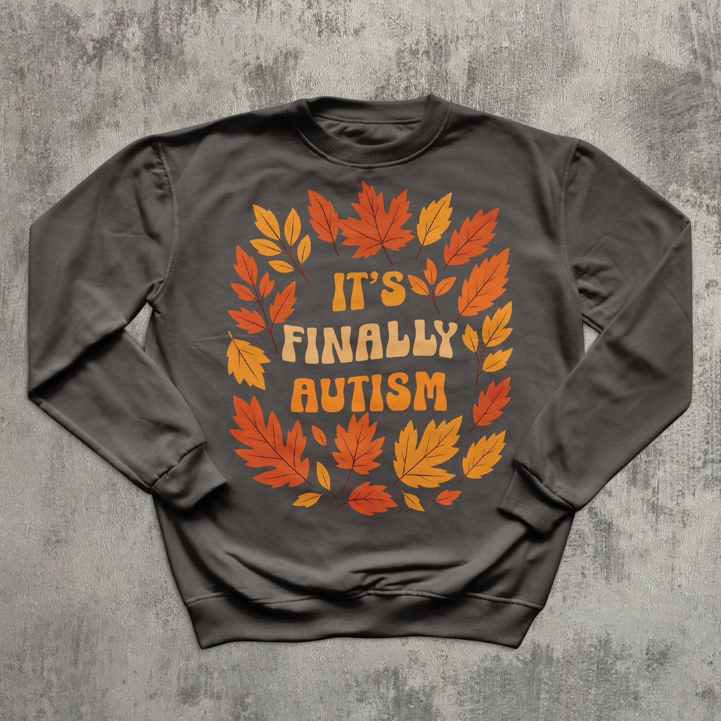 Gray sweatshirt with autumn leaf design and 'It's Finally Autism' text on a textured gray background