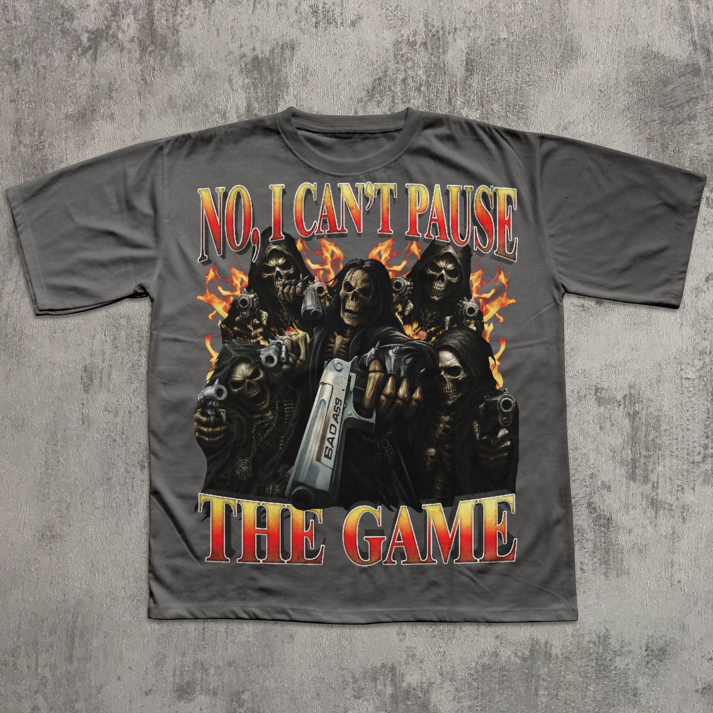 Gray t-shirt with graphic design of skeletons holding guns and a console, text 'No, I Can't Pause The Game' on a textured gray background.