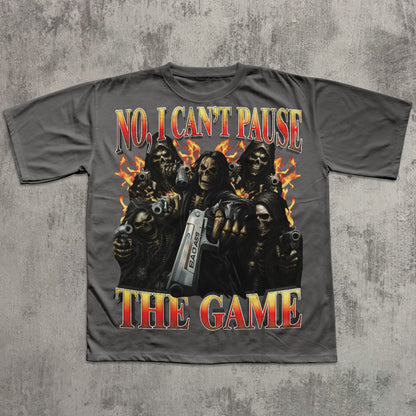 Gray t-shirt with graphic design of skeletons holding guns and a console, text 'No, I Can't Pause The Game' on a textured gray background.
