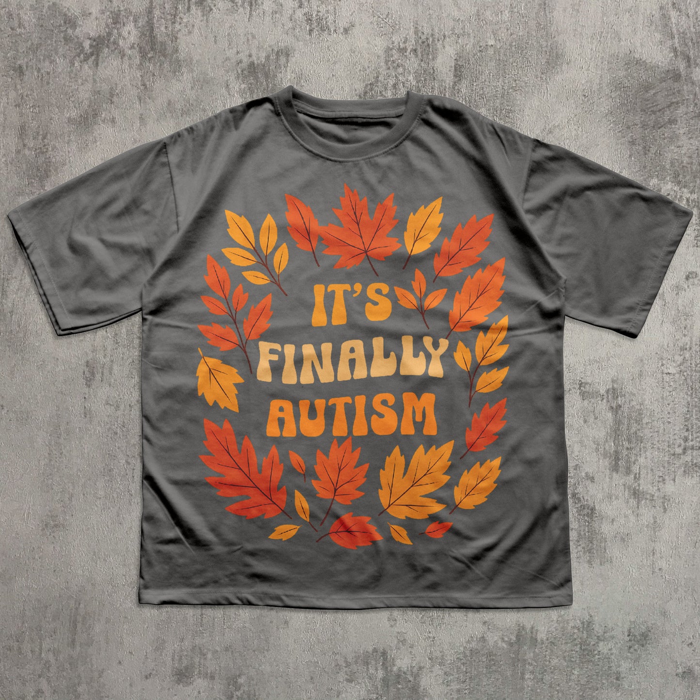 Gray t-shirt with autumn leaf design and 'It's Finally Autism' text on a textured gray background