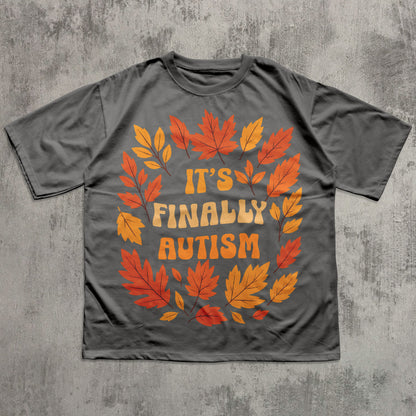 Gray t-shirt with autumn leaf design and 'It's Finally Autism' text on a textured gray background